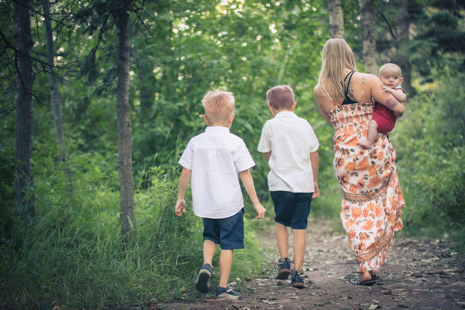 Mother walks with three young children along a forest path in a candid family portrait session.