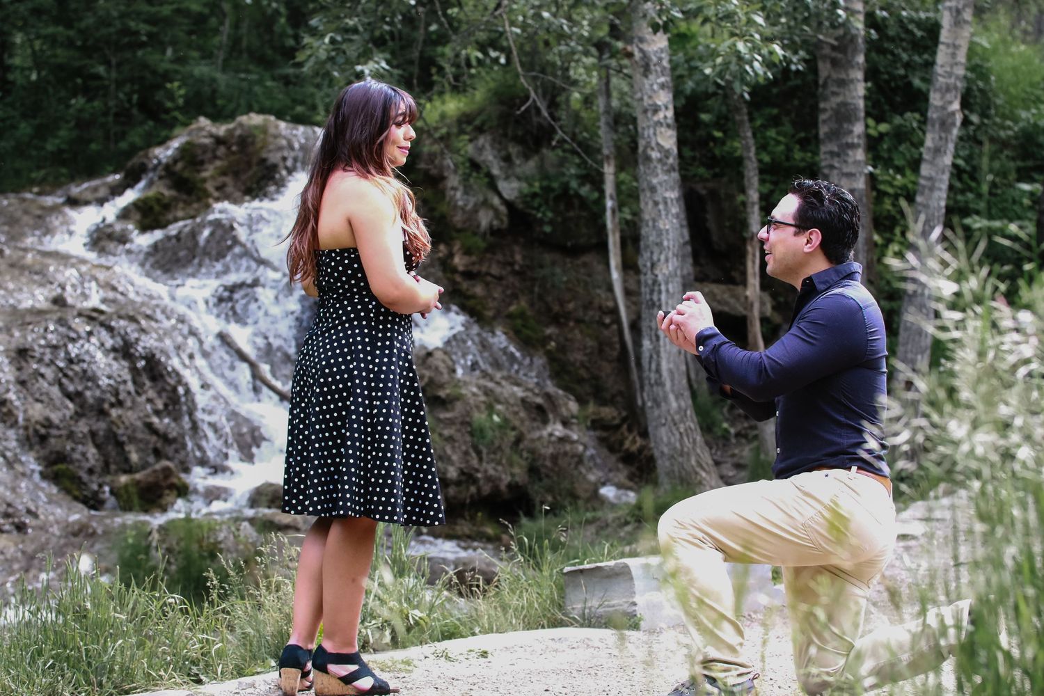 Romantic marriage proposal by a waterfall with man on one knee outdoors.