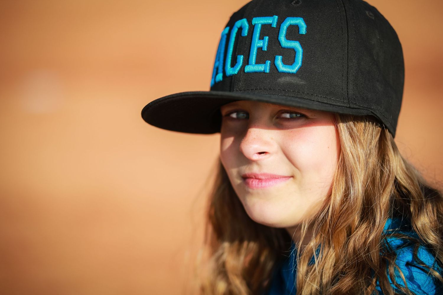 A smiling teenage girl wearing a black Aces snapback cap poses for a close-up portrait.