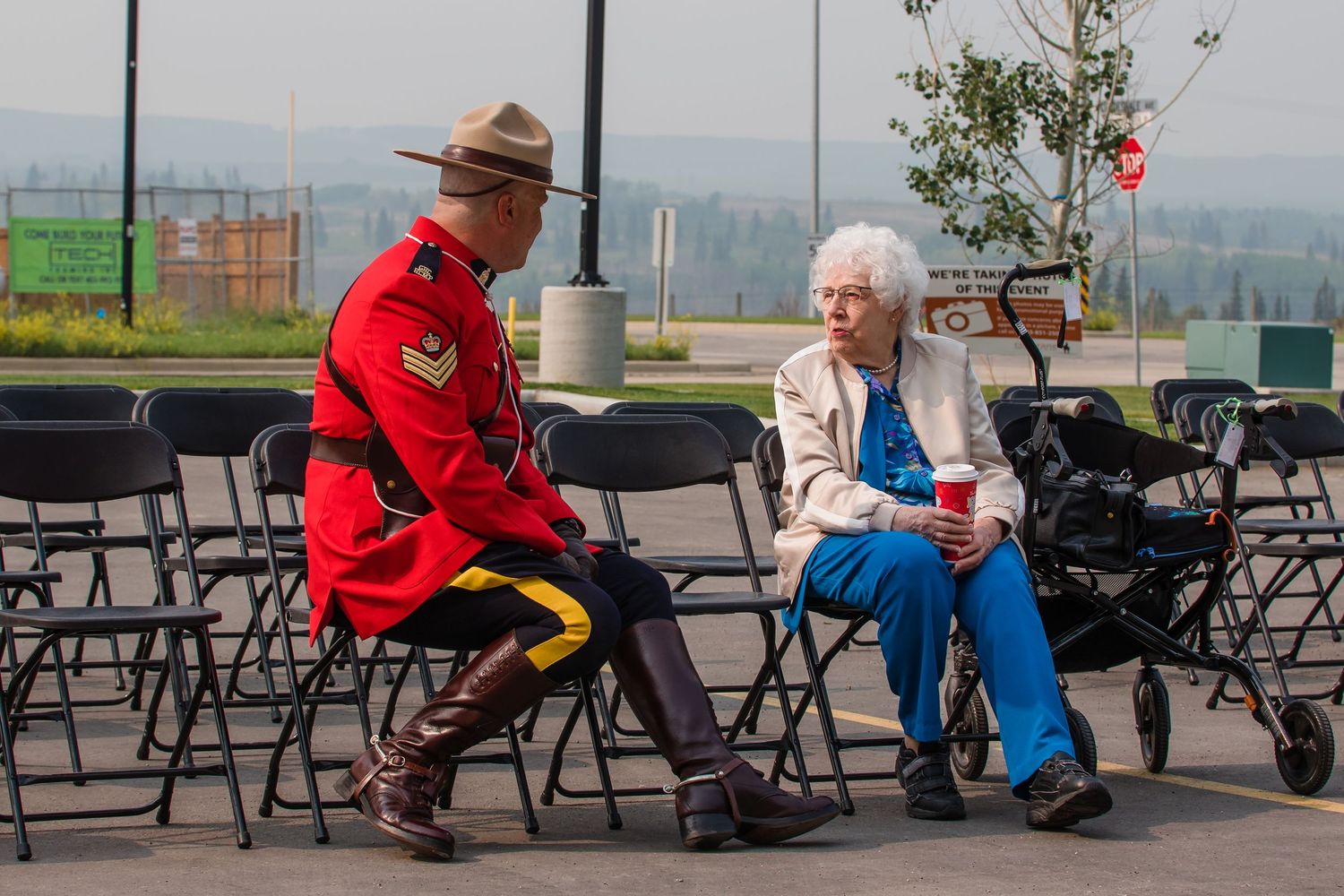 An RCMP officer in red serge uniform chats with an elderly woman at an outdoor event.