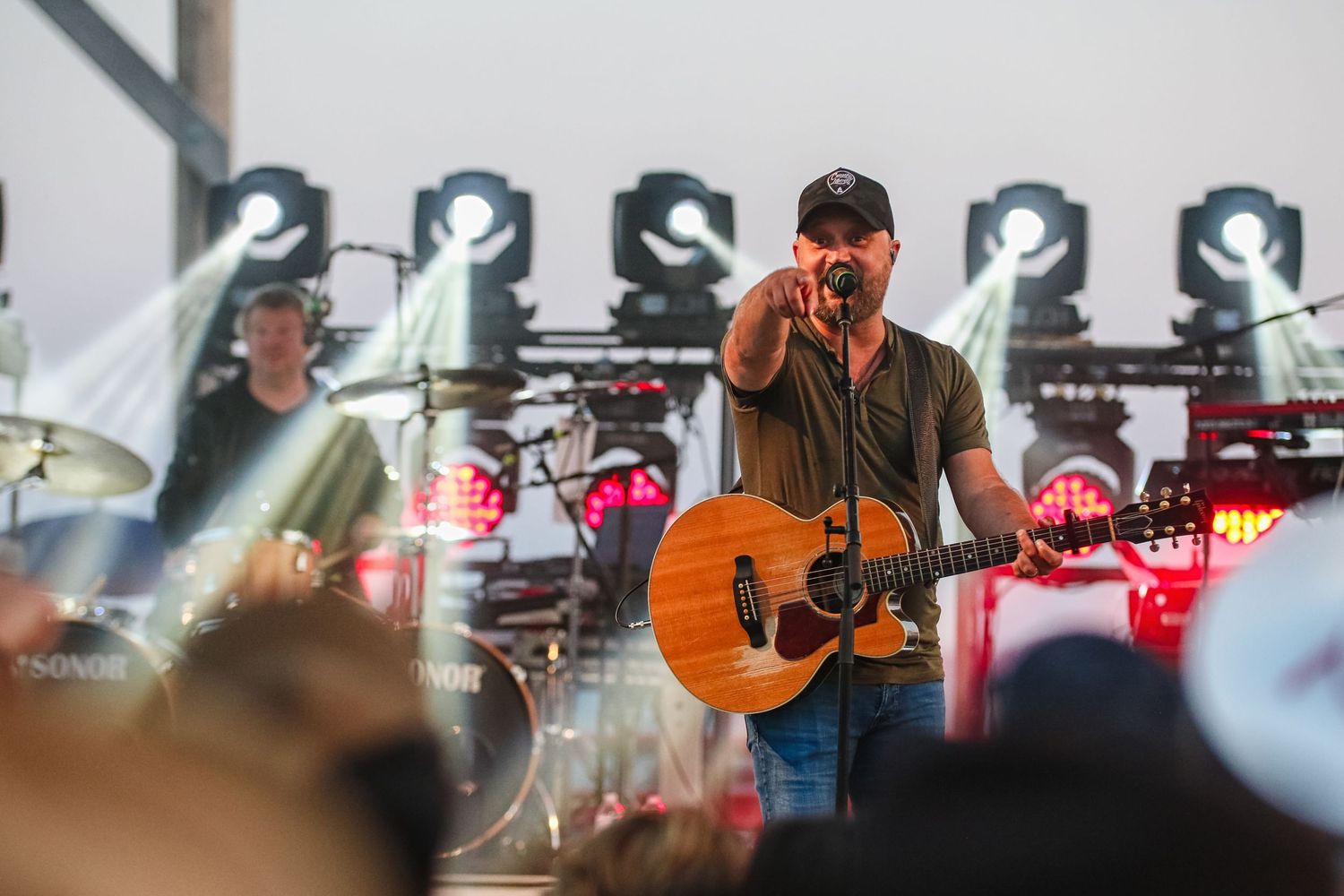 Country music performer plays acoustic guitar on a lit concert stage while pointing at the crowd.