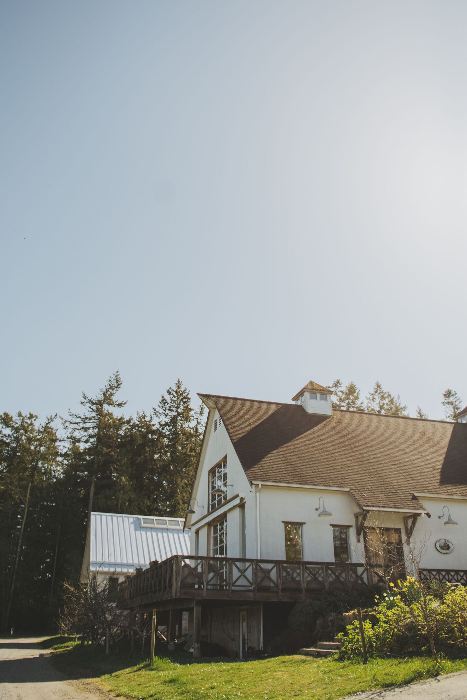 White barn-style wedding venue with wrap-around deck nestled among tall evergreen trees.
