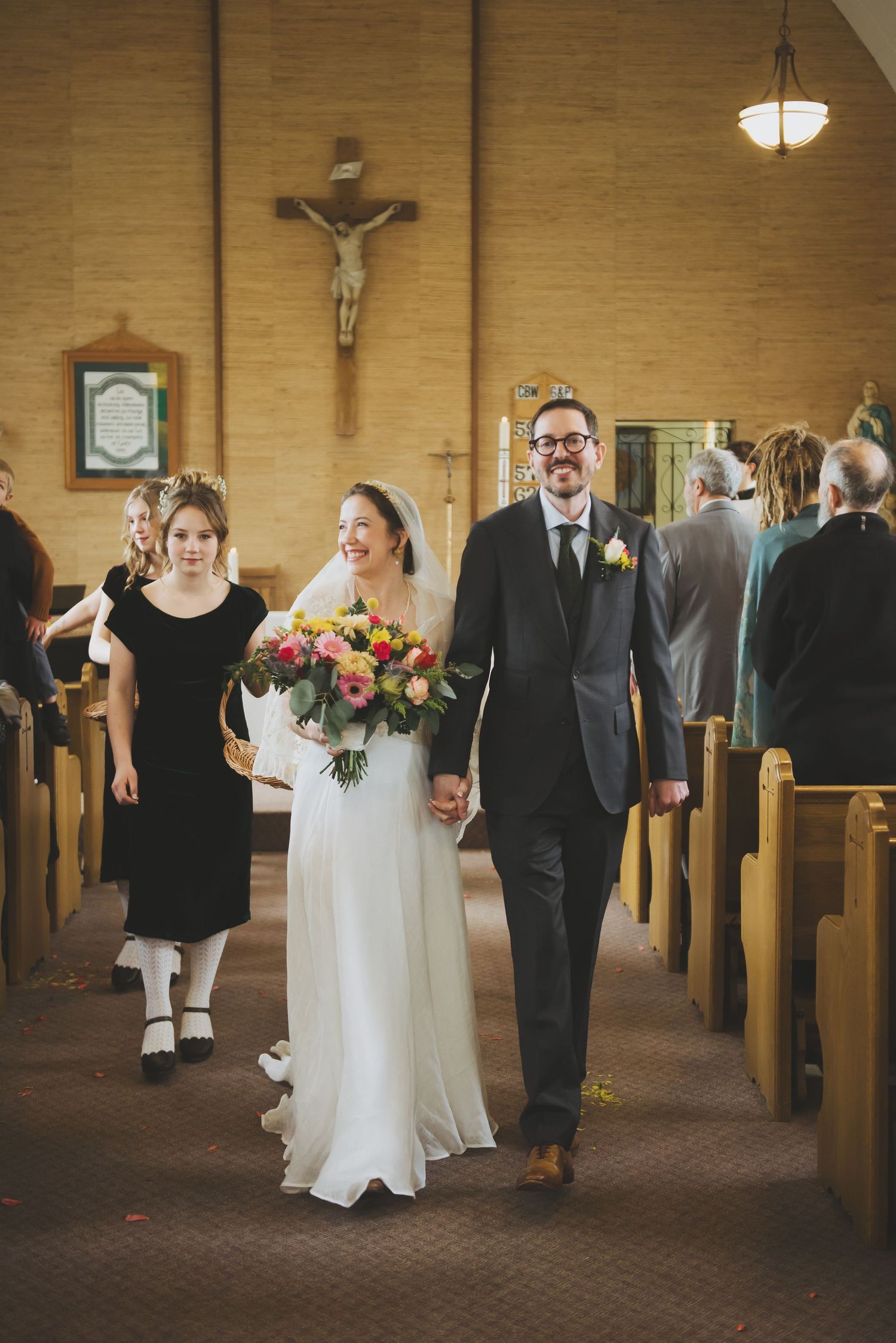 Wedding couple walking down church aisle after ceremony with crucifix visible in background.