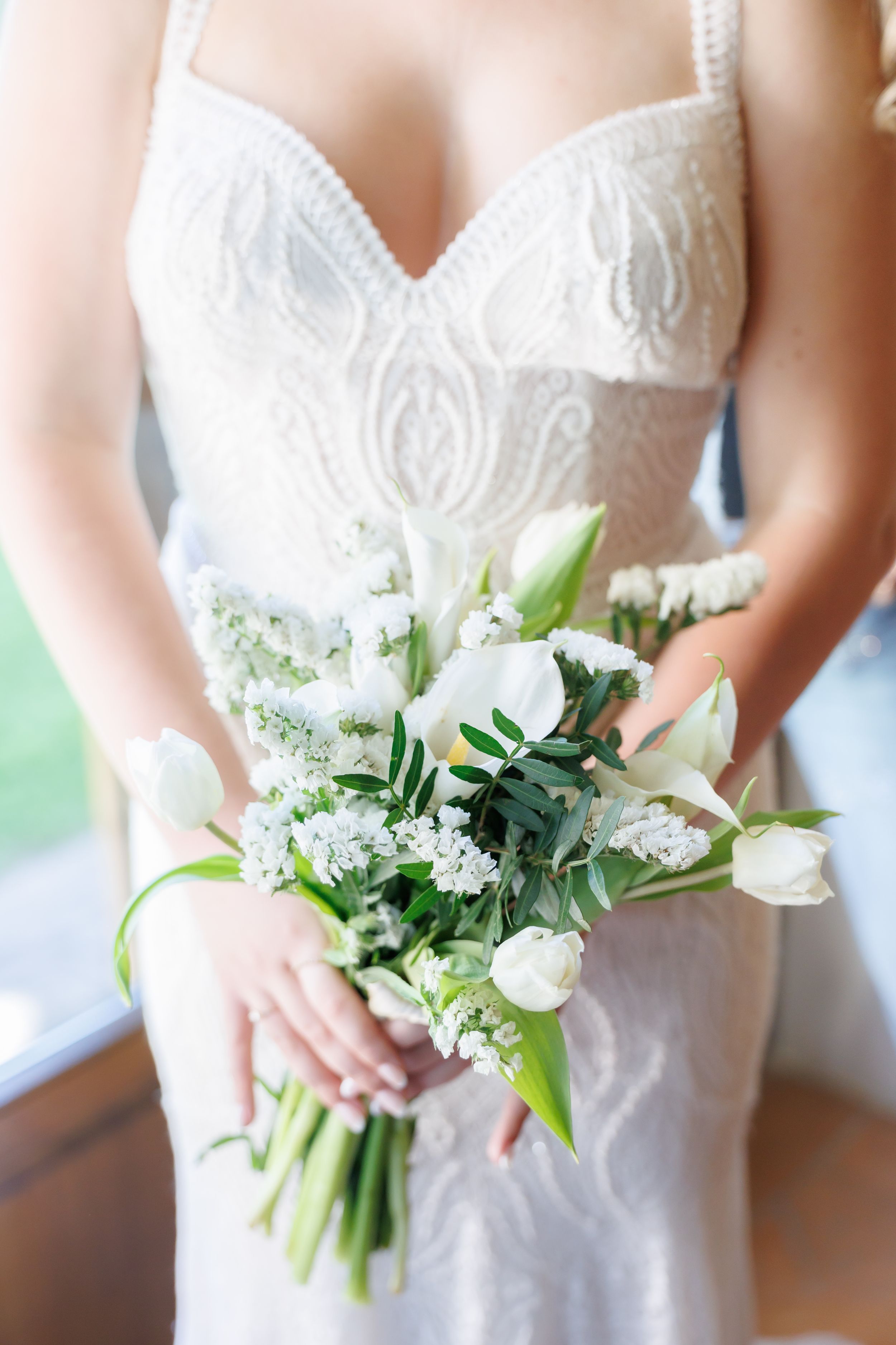 Bride in white lace dress holding elegant bridal bouquet of white tulips and greenery.