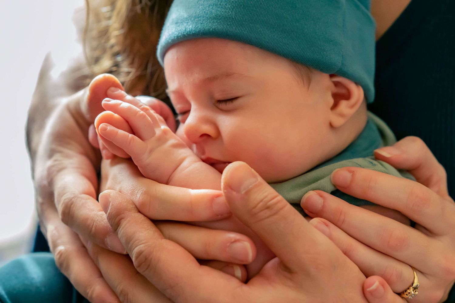 newborn boy in blue surrounded by mom and dad's hands