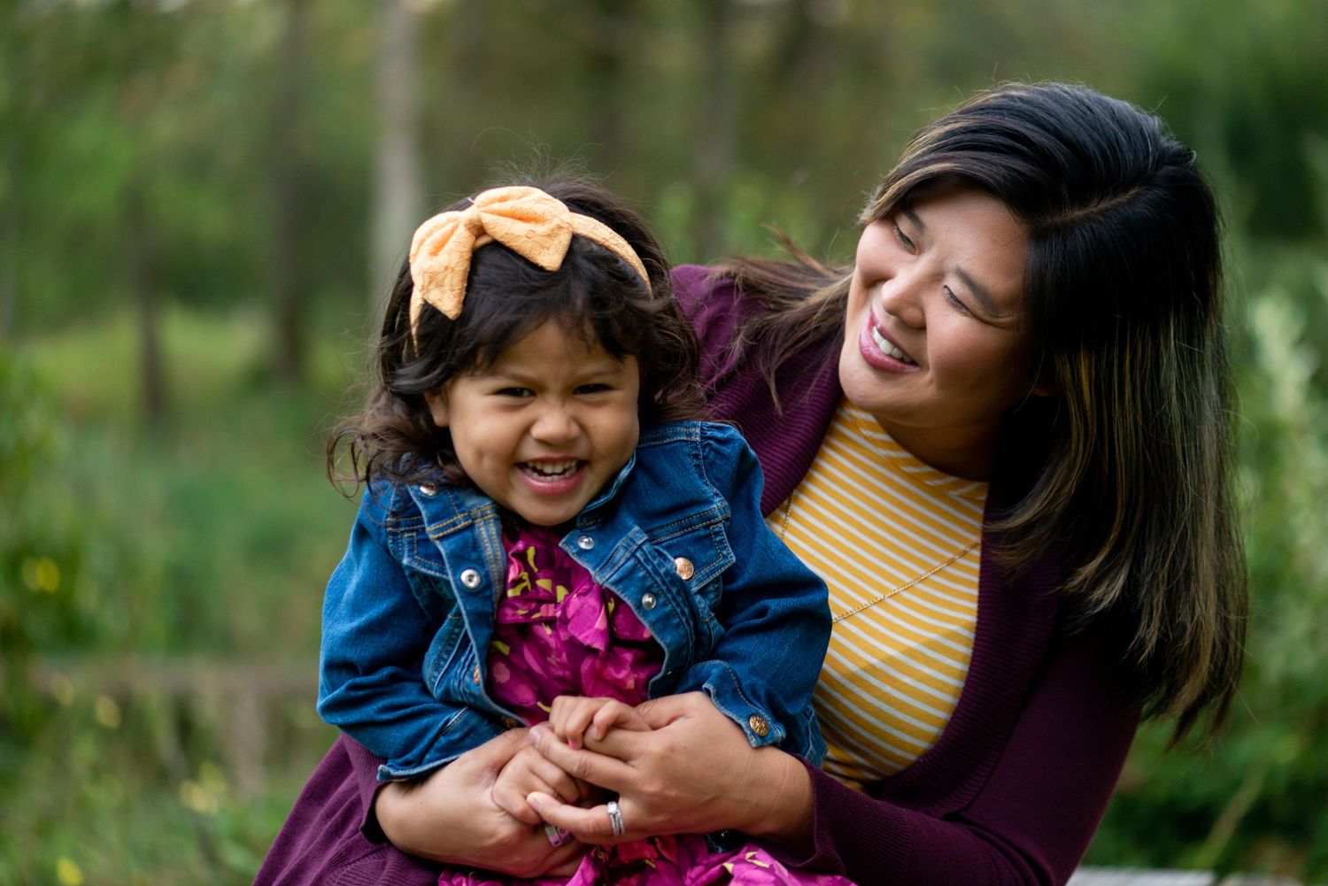 Candid outdoor family moment with mother and daughter laughing in a garden setting.