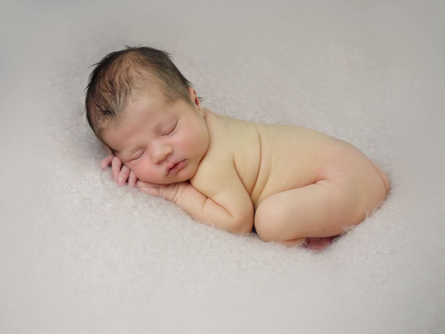 newborn baby girl laying on pink blanket with hands under face
