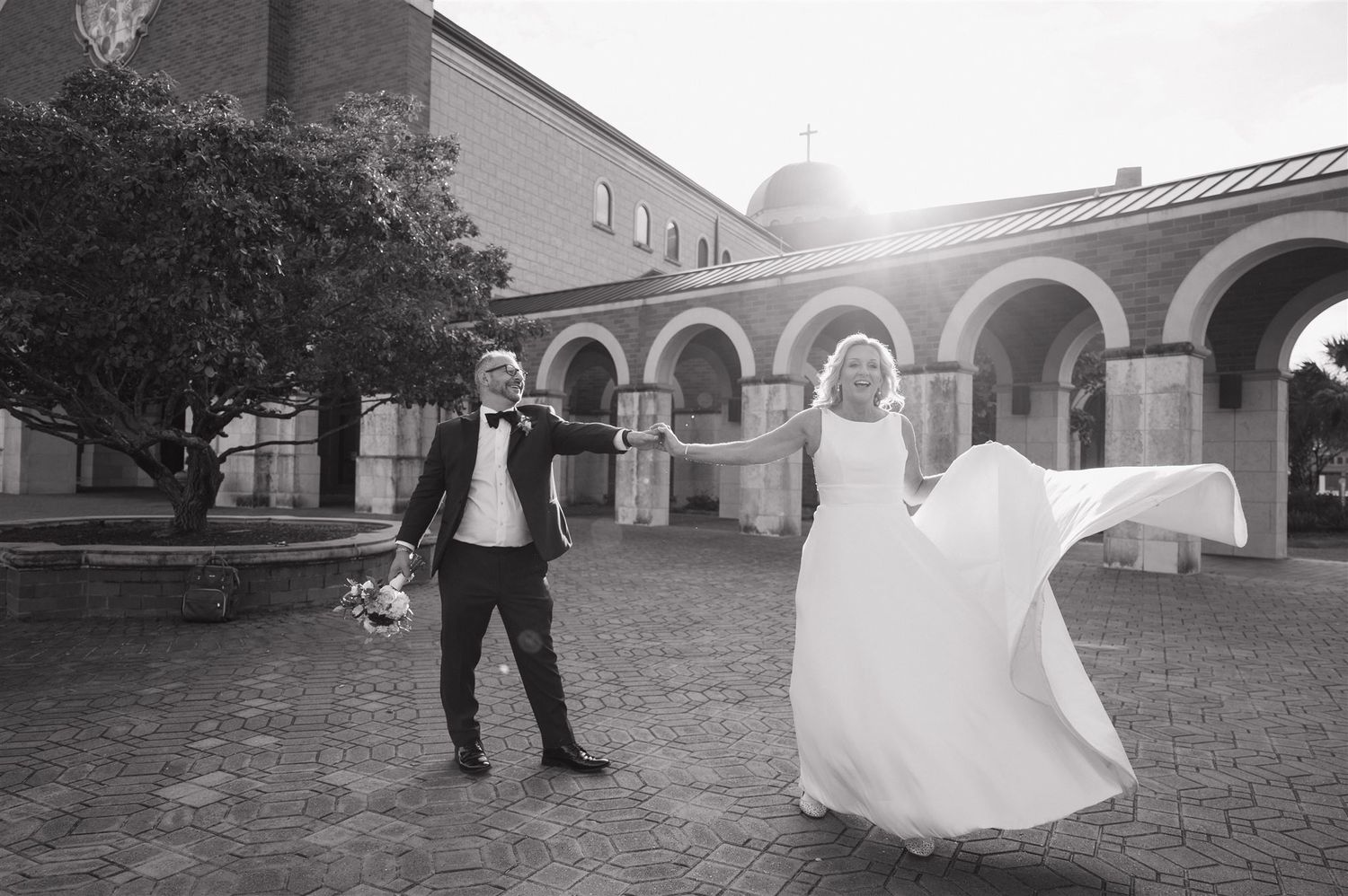 Couple dances playfully under arched colonnade in black and white photography.