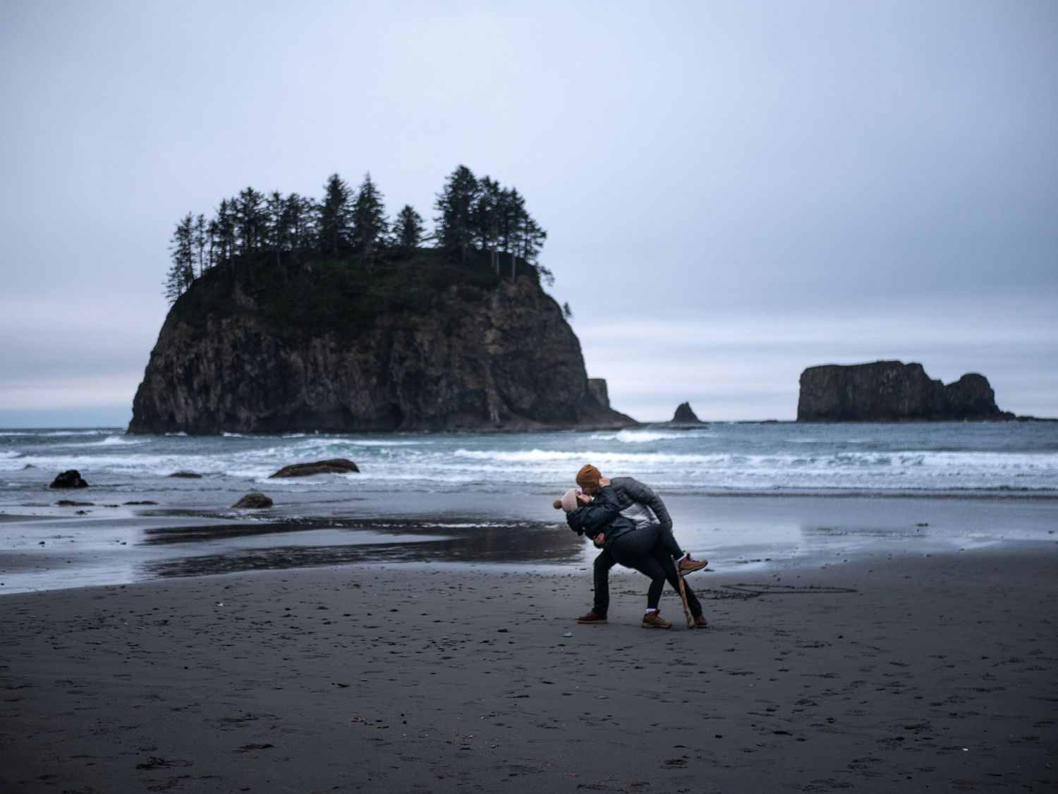 A photographer captures images on a moody Pacific Northwest beach with sea stacks.