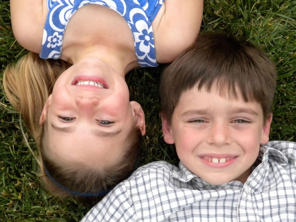 Two children lying head-to-head on grass smiling at camera.
