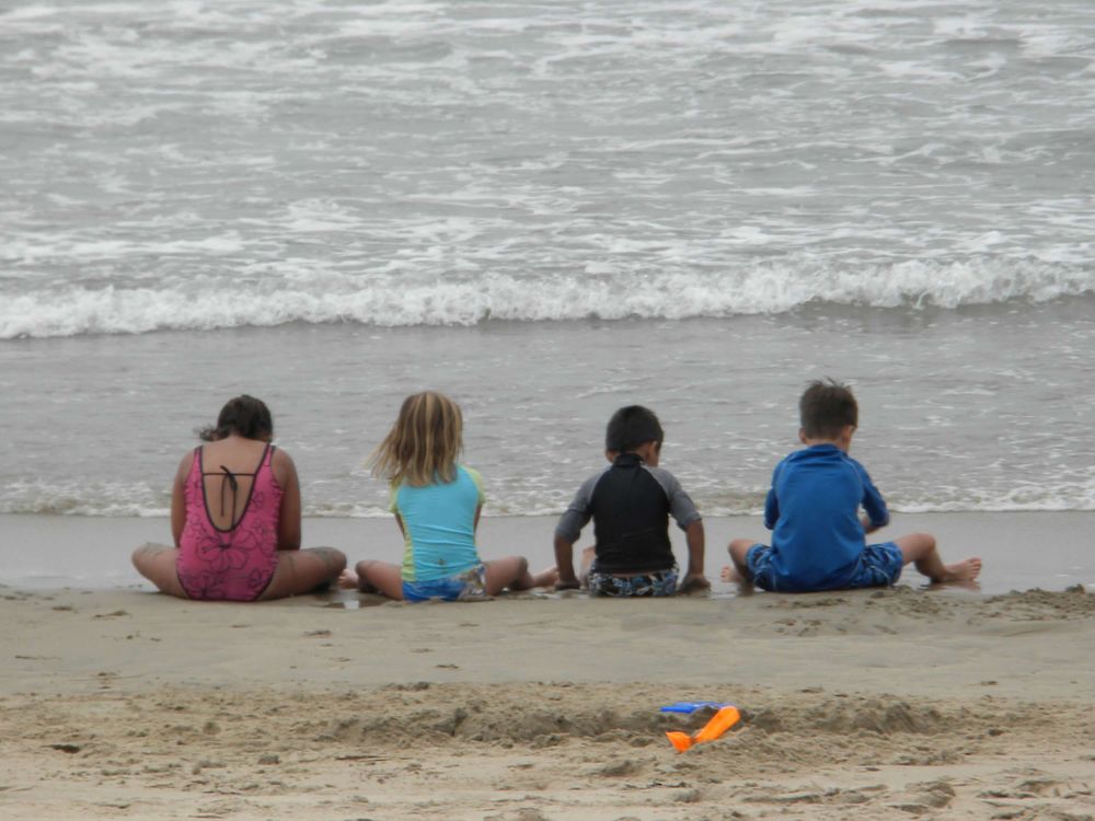 Four people sitting on beach watching waves roll in.