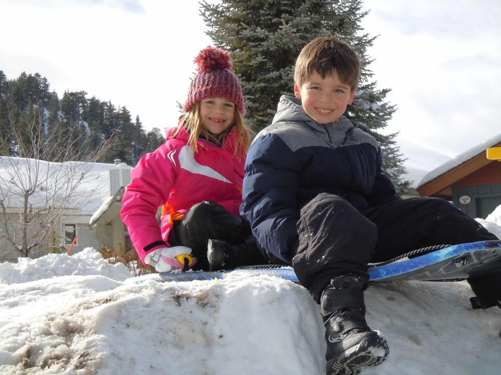 Two children sitting on snowy hill in winter gear.