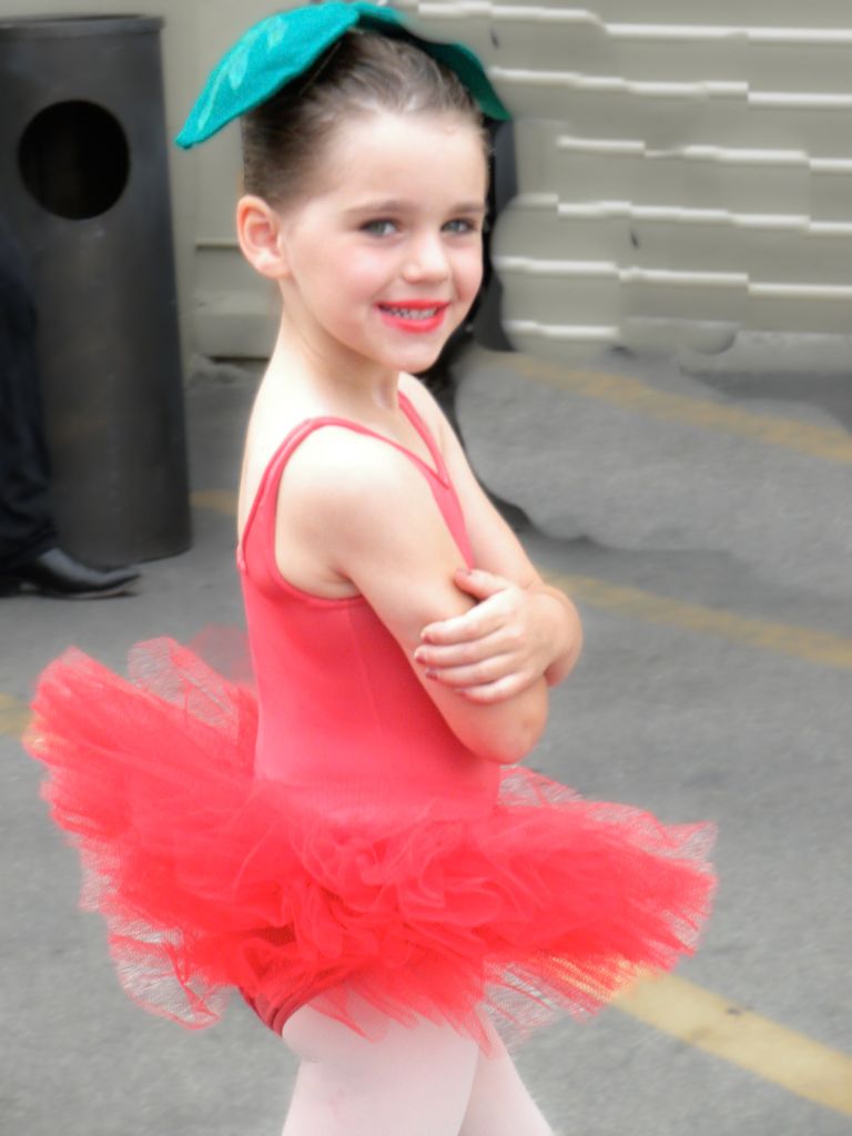 Young dancer in red tutu and mint headband poses backstage.