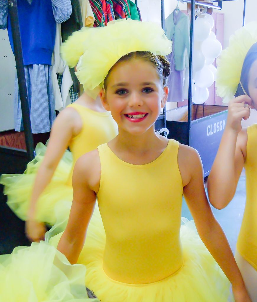Young performer in bright yellow tutu costume backstage at dance recital.