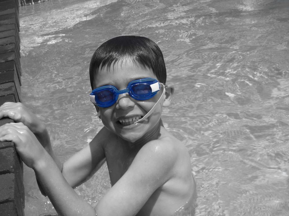 Child wearing blue goggles smiling in swimming pool.