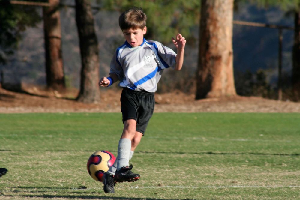 Young soccer player in white jersey kicking ball during game on grass field.