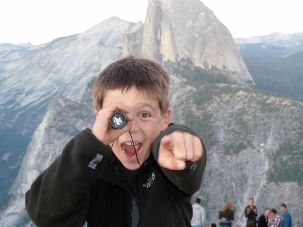 Child making silly face with Half Dome mountain peak visible in background at Yosemite.