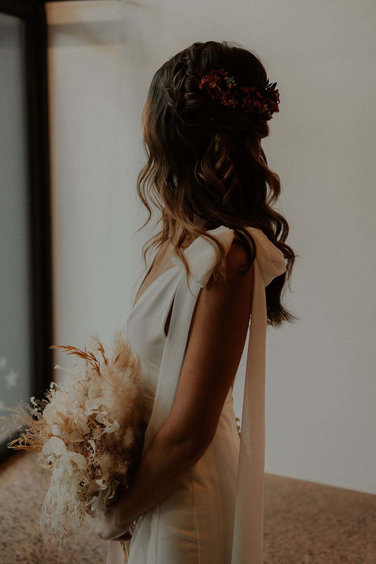 Side profile of bride in white dress with braided hairstyle and dried flower bouquet.