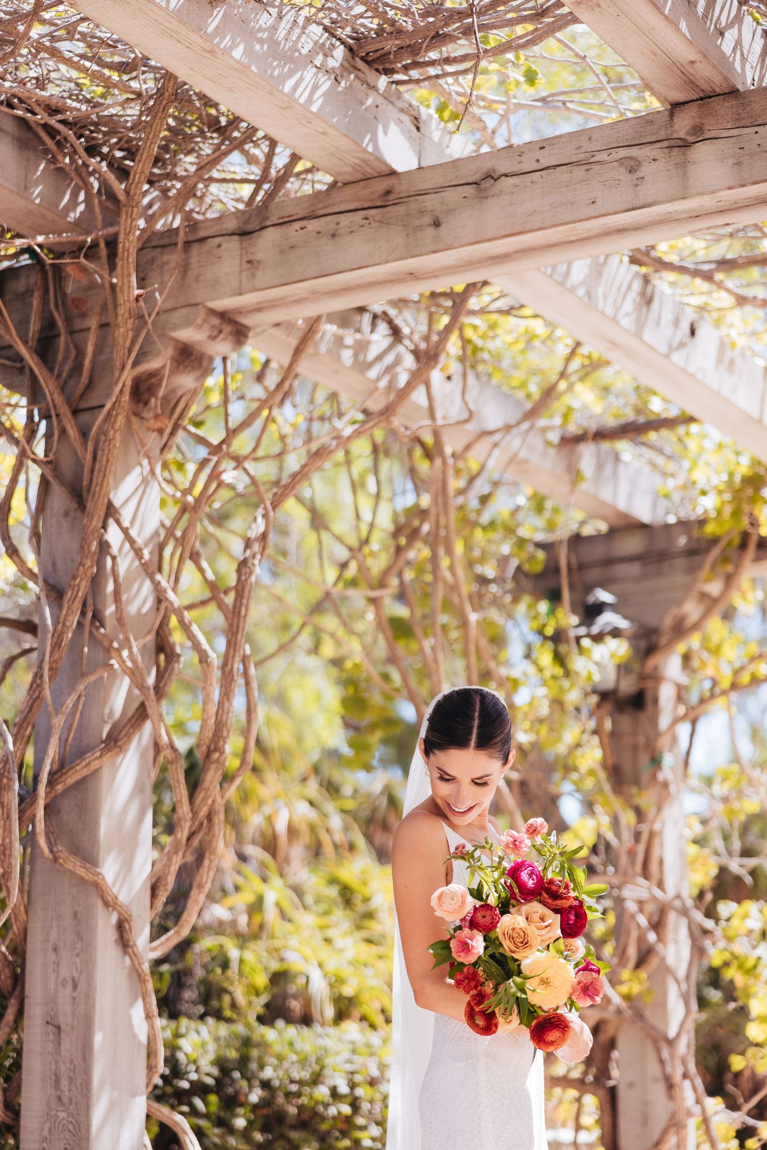 Bridal portrait under a wooden pergola with pink and red bouquet.