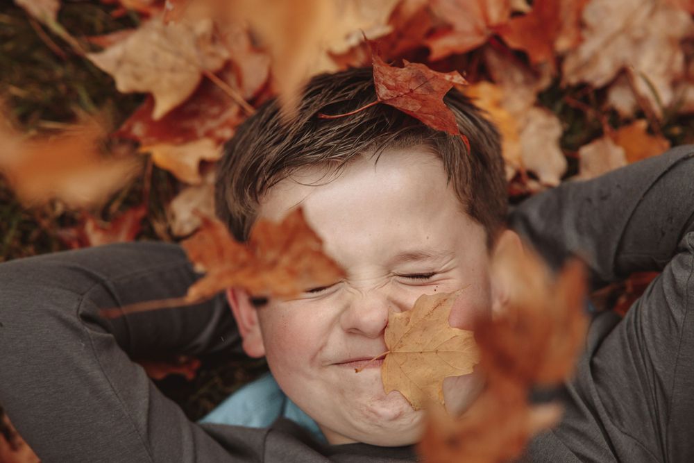 A boy lies on the ground surrounded by colorful autumn leaves, enjoying a moment of nature's beauty.