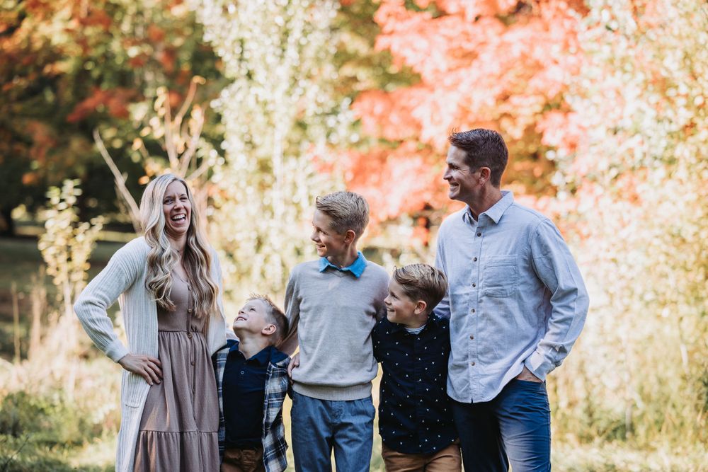 A family smiles together for a photo in a colorful autumn park filled with fallen leaves.