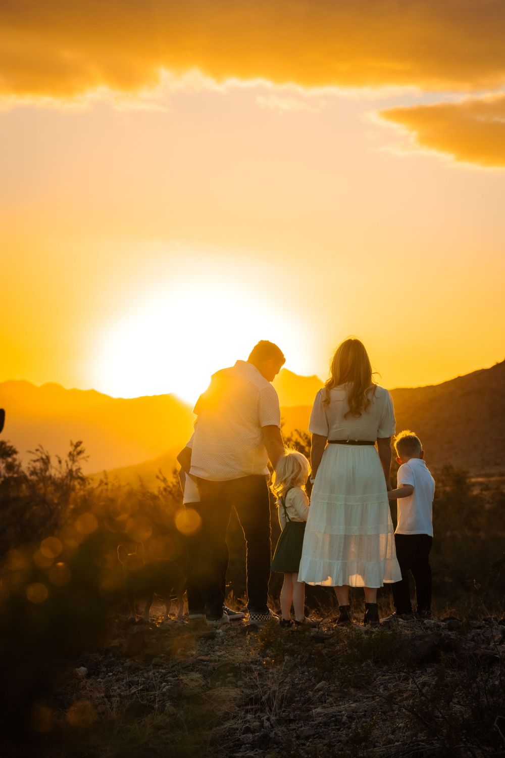 A family stands together in the desert, silhouetted against a vibrant sunset sky.
