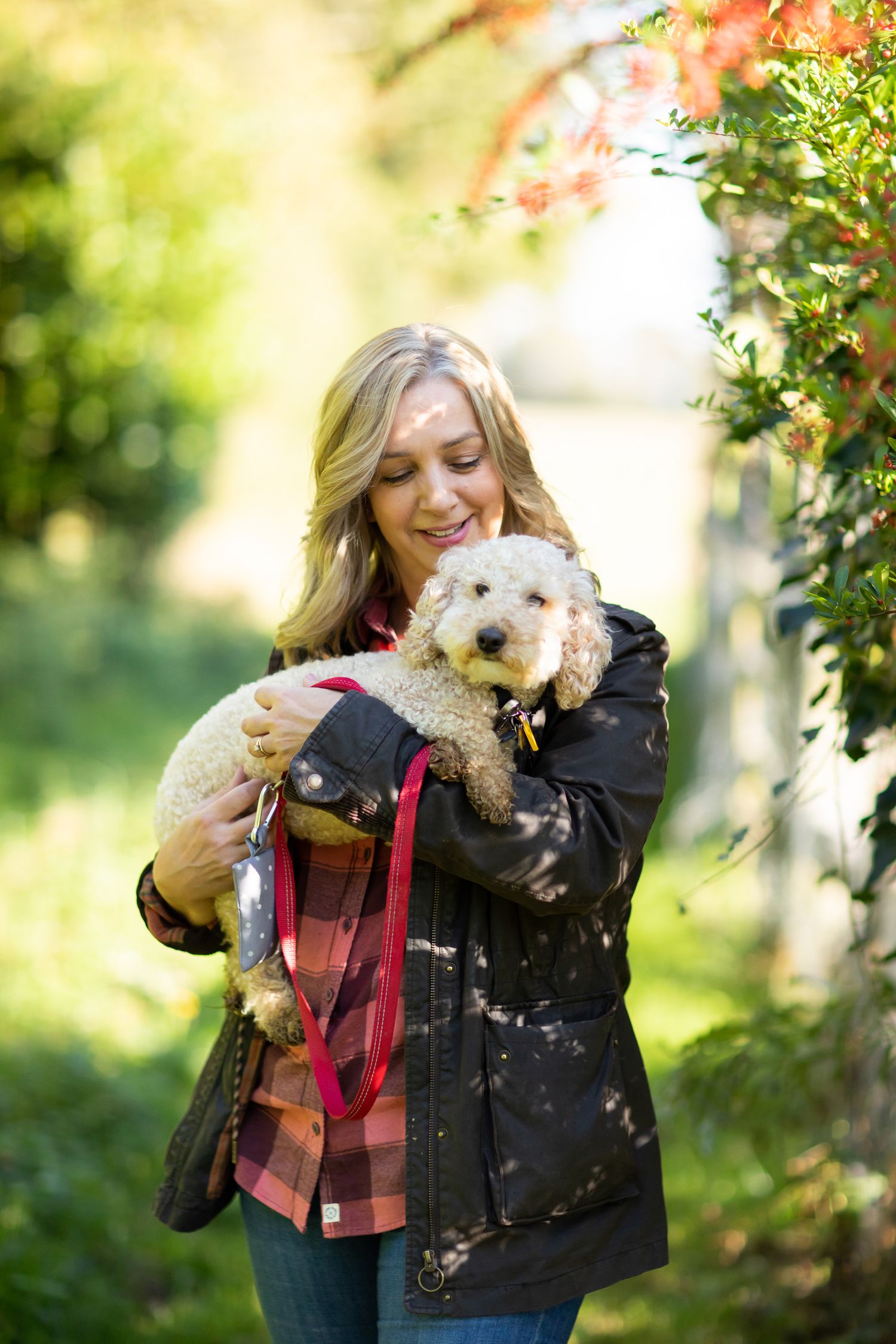 A person holds a small white fluffy dog while standing outdoors among autumn foliage during business branding photoshoot.