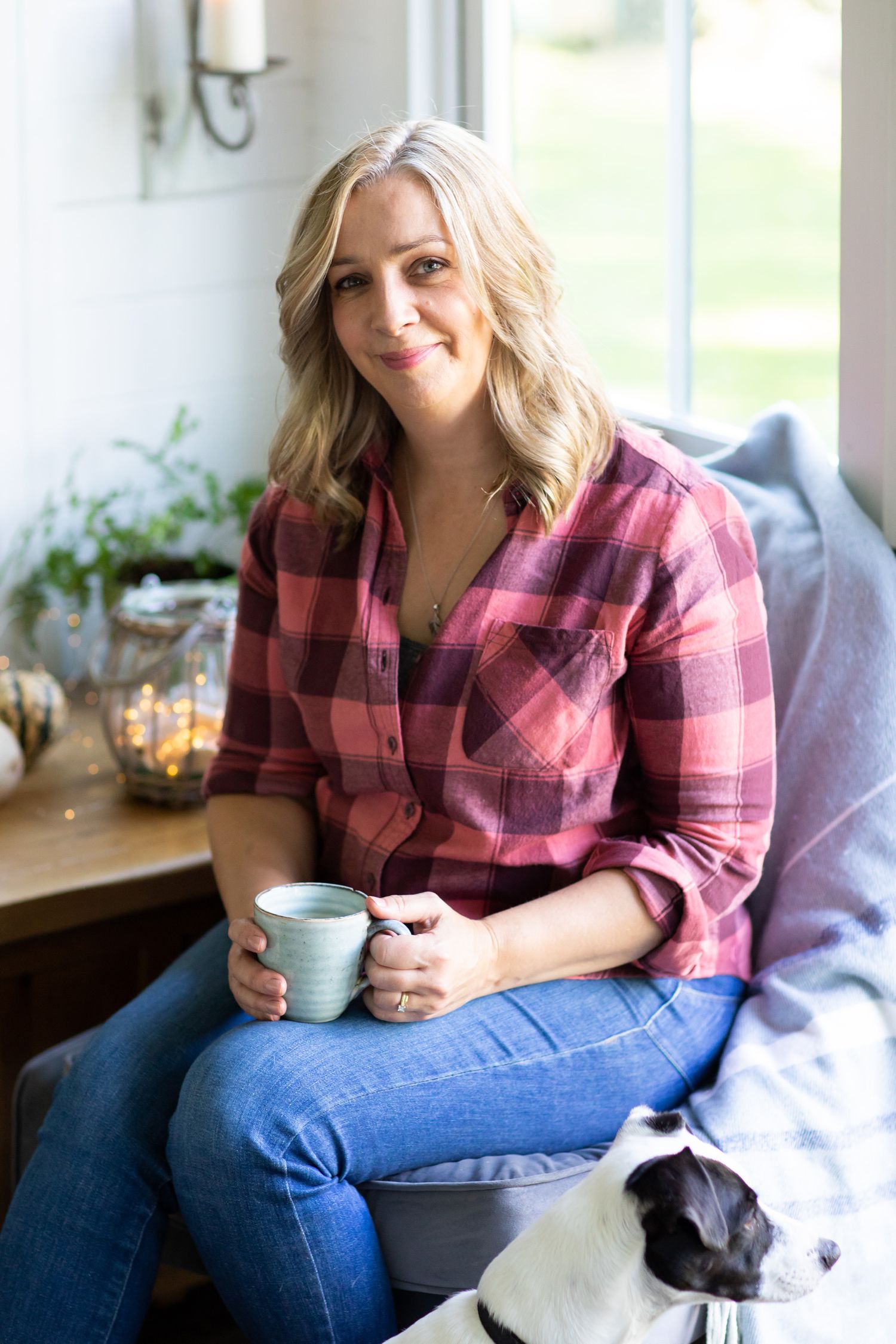 A person relaxes at home in a plaid shirt holding a coffee mug while sitting near a window during business branding photoshoot.