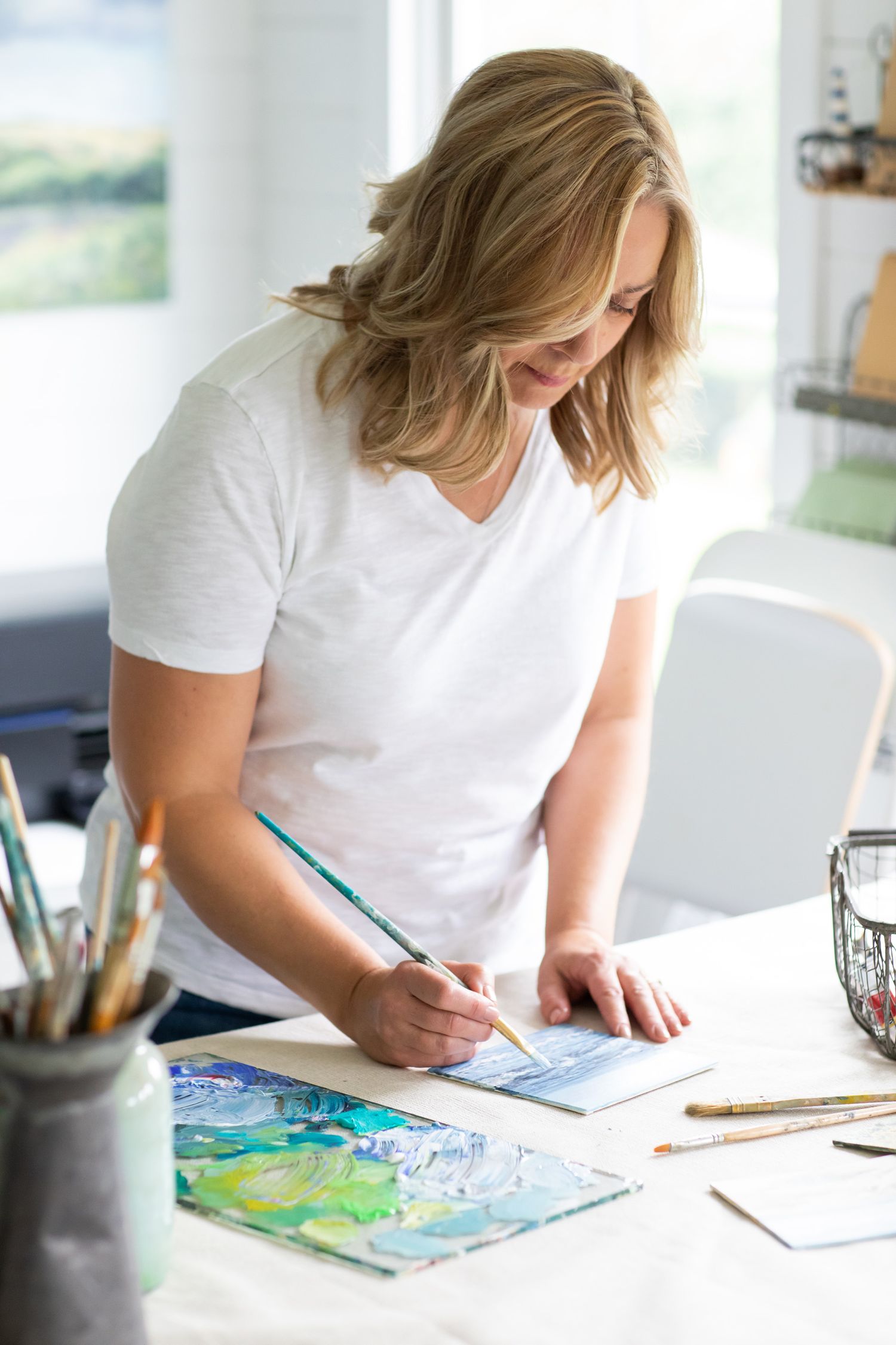 An artist works on a watercolor painting at a white desk with art supplies during business branding photoshoot.