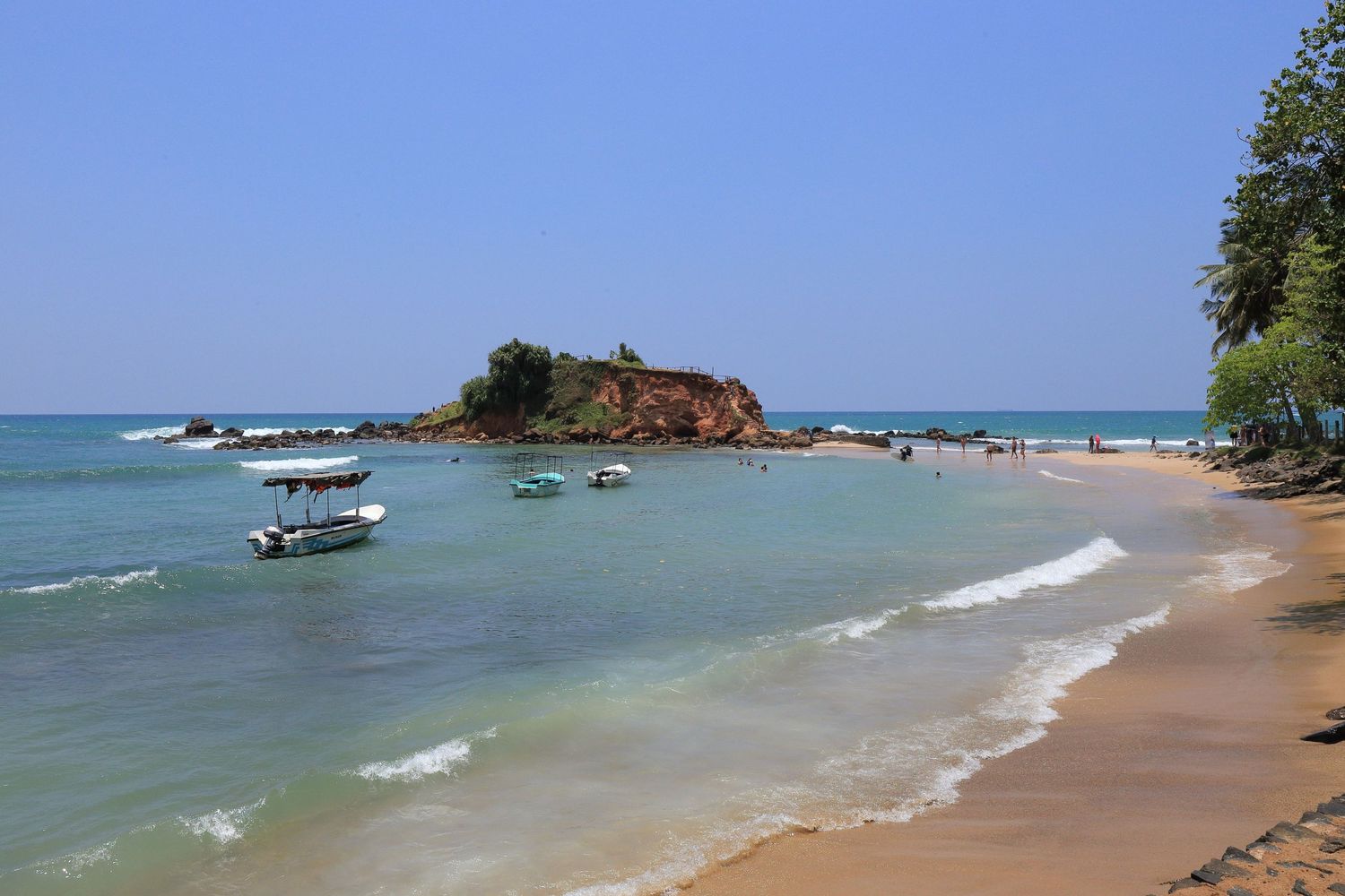 Tranquil beach cove with turquoise waters, rocky outcrops, and a small boat near the shore.