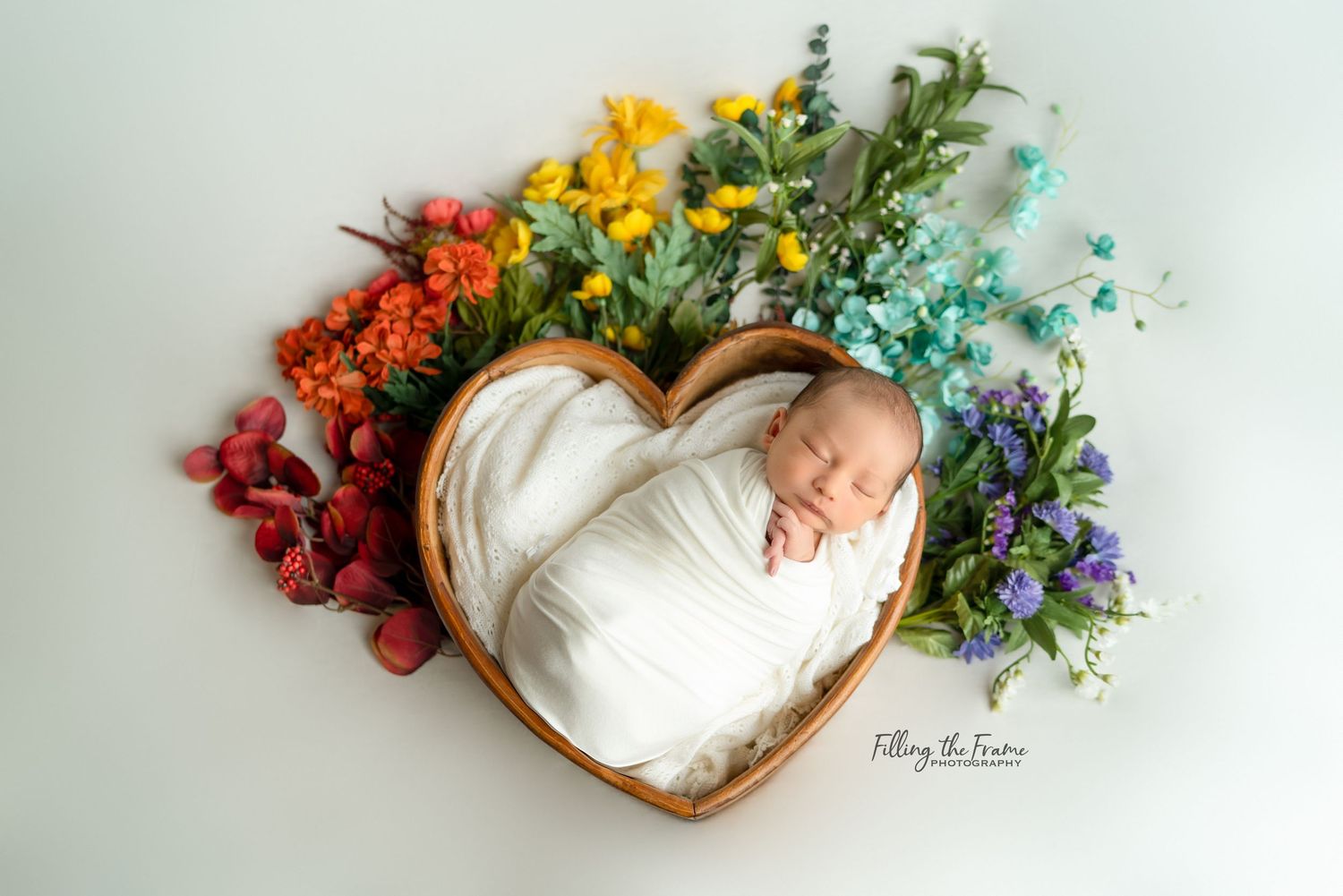 Newborn baby sleeping peacefully surrounded by colorful flowers and greenery.