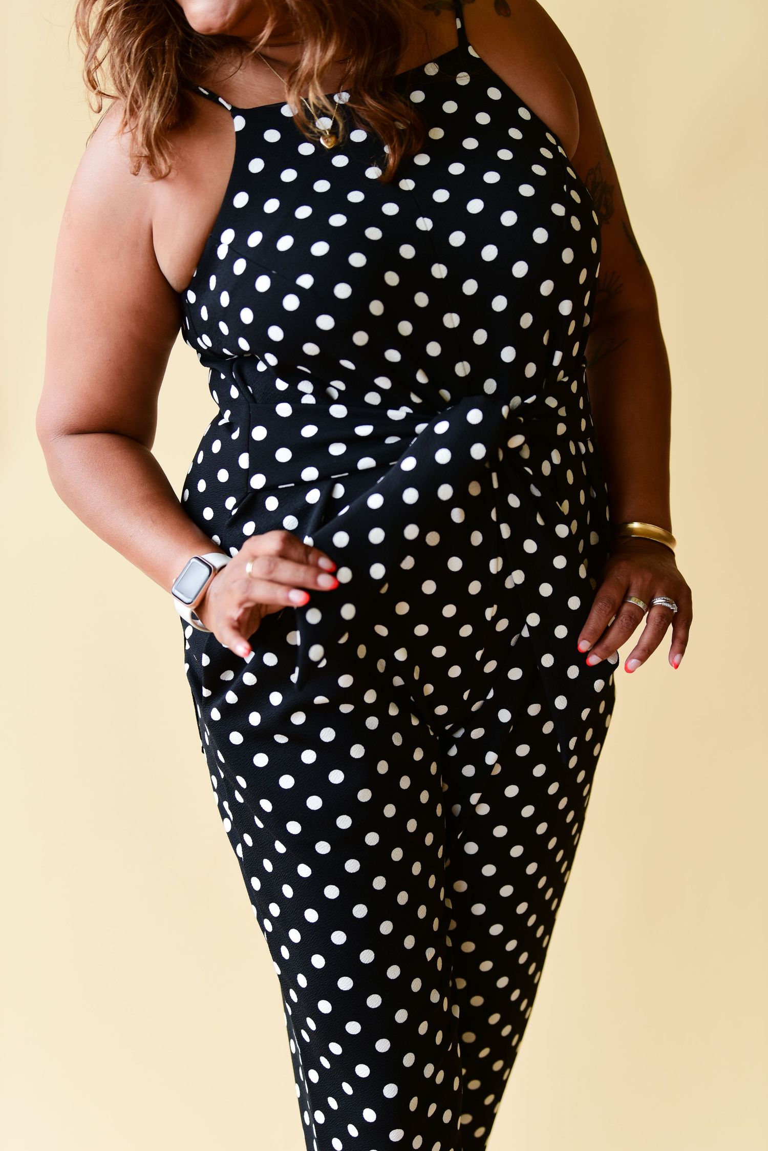 Classic polka dot jumpsuit with fitted waist and straight leg design shown against beige background.