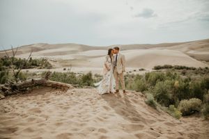 Desert wedding photography session with sand dunes and desert brush creating a dramatic landscape.