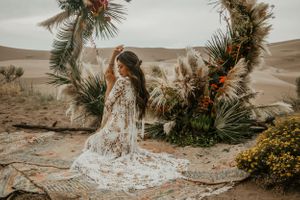 Desert wedding setup with palm fronds and floral arrangements against a sandy backdrop.