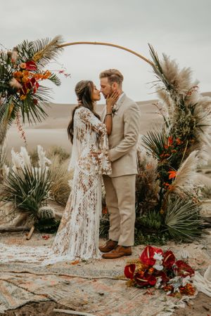 Wedding ceremony setup in desert with floral arch, pampas grass, and red flower arrangements.
