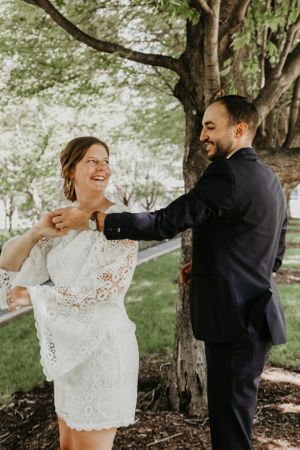 A couple dances and twirls under trees in a garden setting.