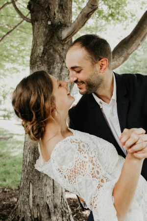 A couple shares a romantic dance moment under green trees.