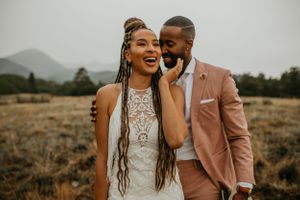 A happy couple in wedding attire laughing together in a natural landscape.