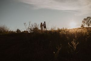 A couple walks along a hilltop path at sunset creating silhouettes against the golden sky.