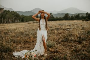 A stunning bridal portrait in a white lace gown with a thigh slit against a mountain landscape at sunset.