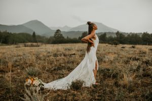 Elegant wedding dress with flowing train photographed in a golden field with mountains in the background.