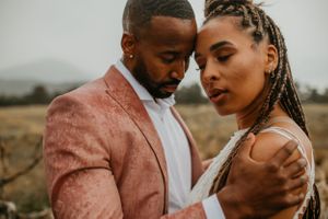 Intimate couple portrait featuring a pink suit jacket and elegant formal attire in a natural setting.