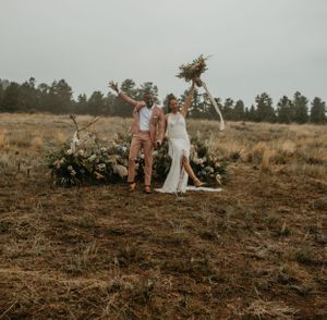 Wedding couple celebrating with raised arms in an outdoor mountain setting at sunset.