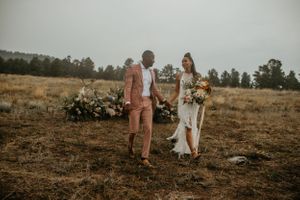 A couple poses together in an open field with mountains and trees in the background.