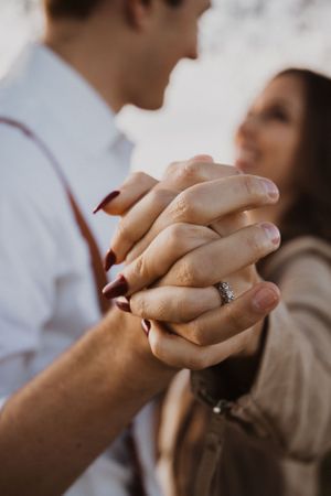 Close-up of clasped hands showing engagement ring in soft lighting.