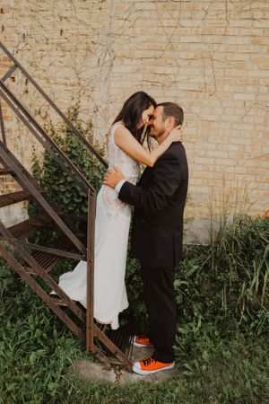 Couple sharing romantic moment by vintage brick wall and metal staircase.