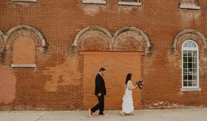 Wedding party walking along rustic brick building exterior.