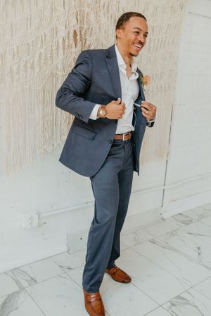 Person in navy suit and brown shoes poses dynamically against white backdrop.
