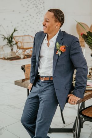 Person in blue suit with coral boutonniere sits casually in modern setting.
