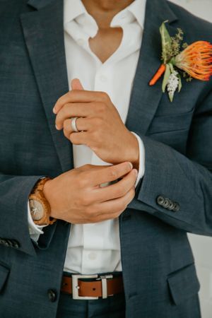 Close-up of hands and coral boutonniere on navy suit with white shirt.